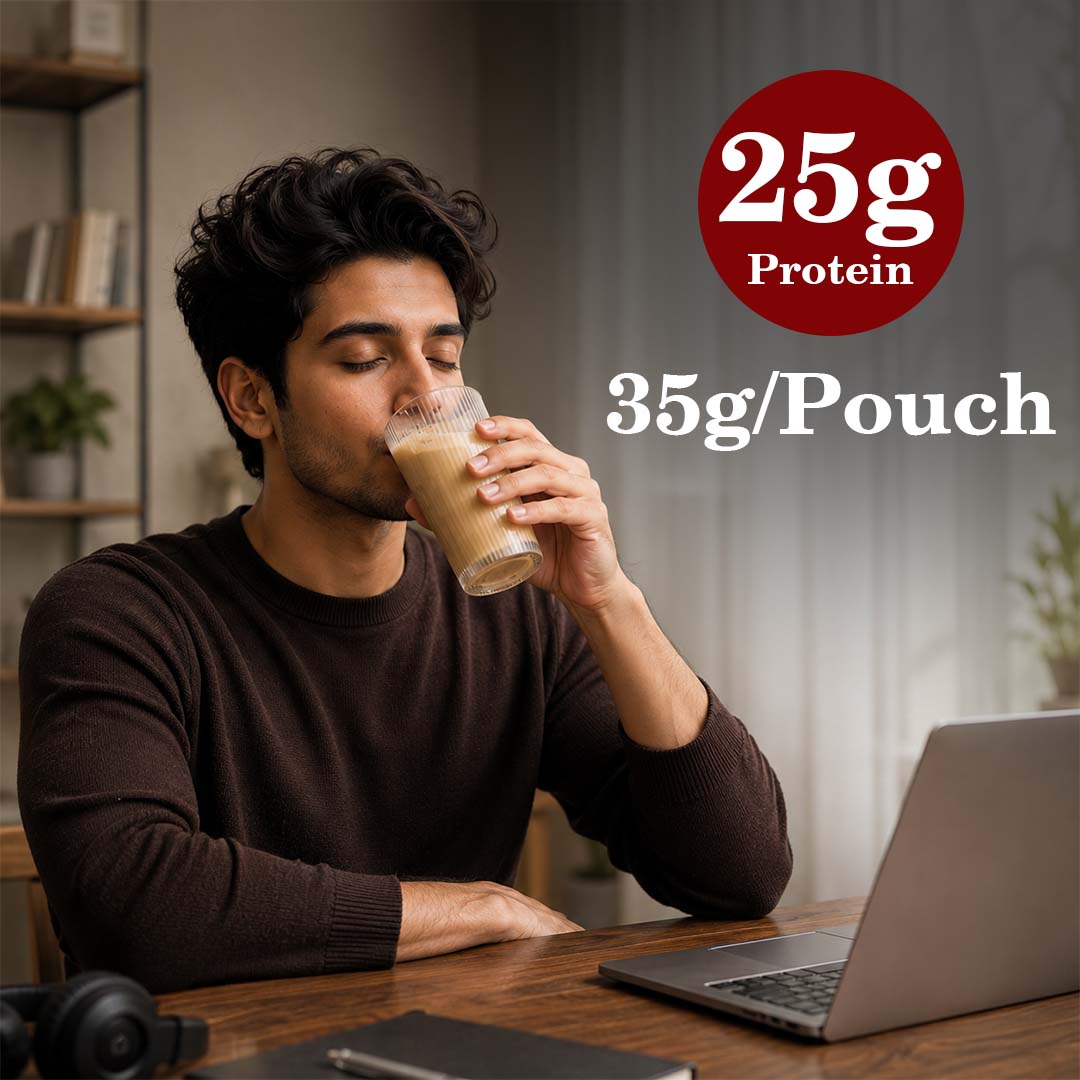 Barsana Magic and A man sitting at a desk drinking a protein shake from a clear plastic cup. He is wearing a dark brown long-sleeve shirt, with a laptop in front of him.