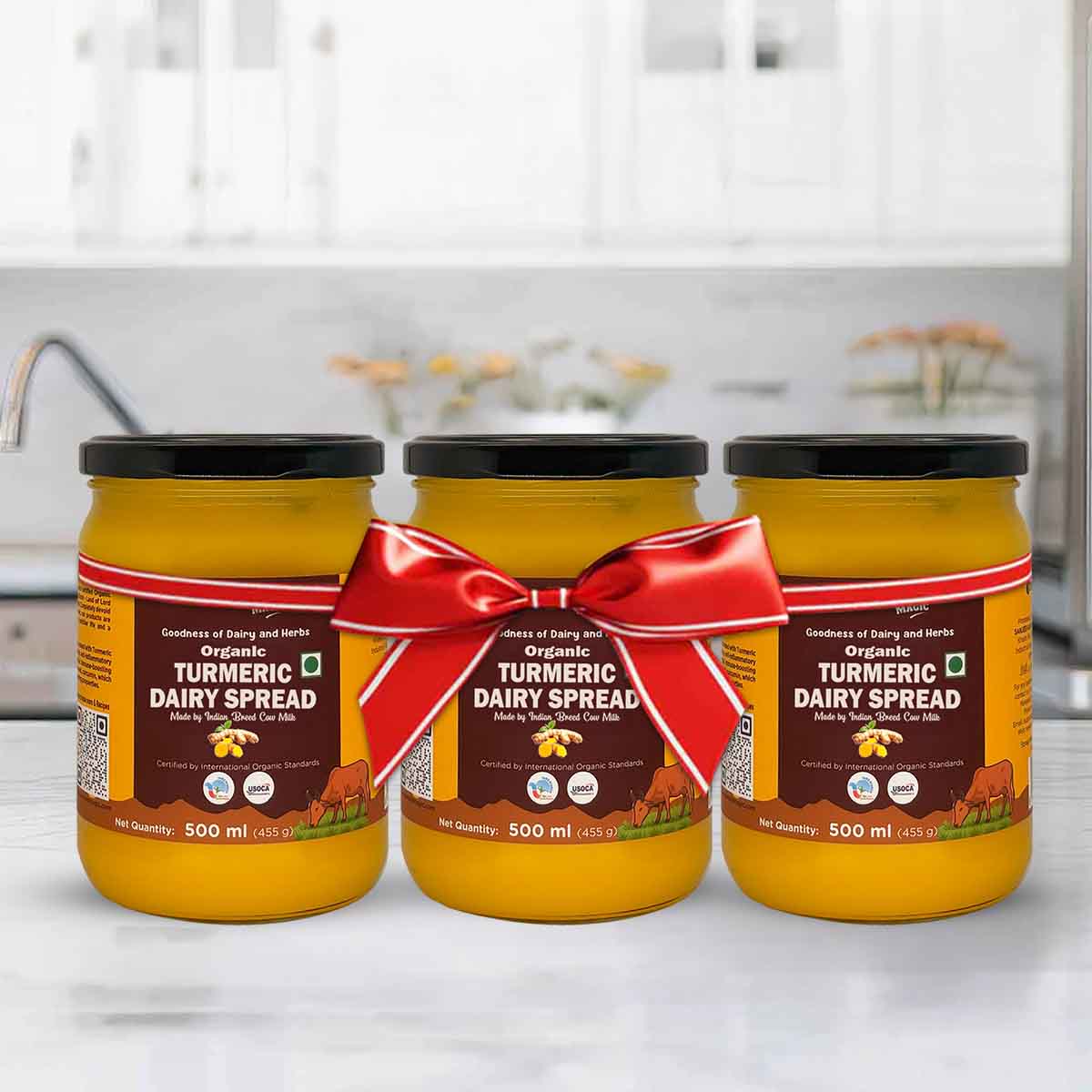Barsana Magic and Three jars of organic turmeric dairy spread with a red ribbon on a kitchen counter.
