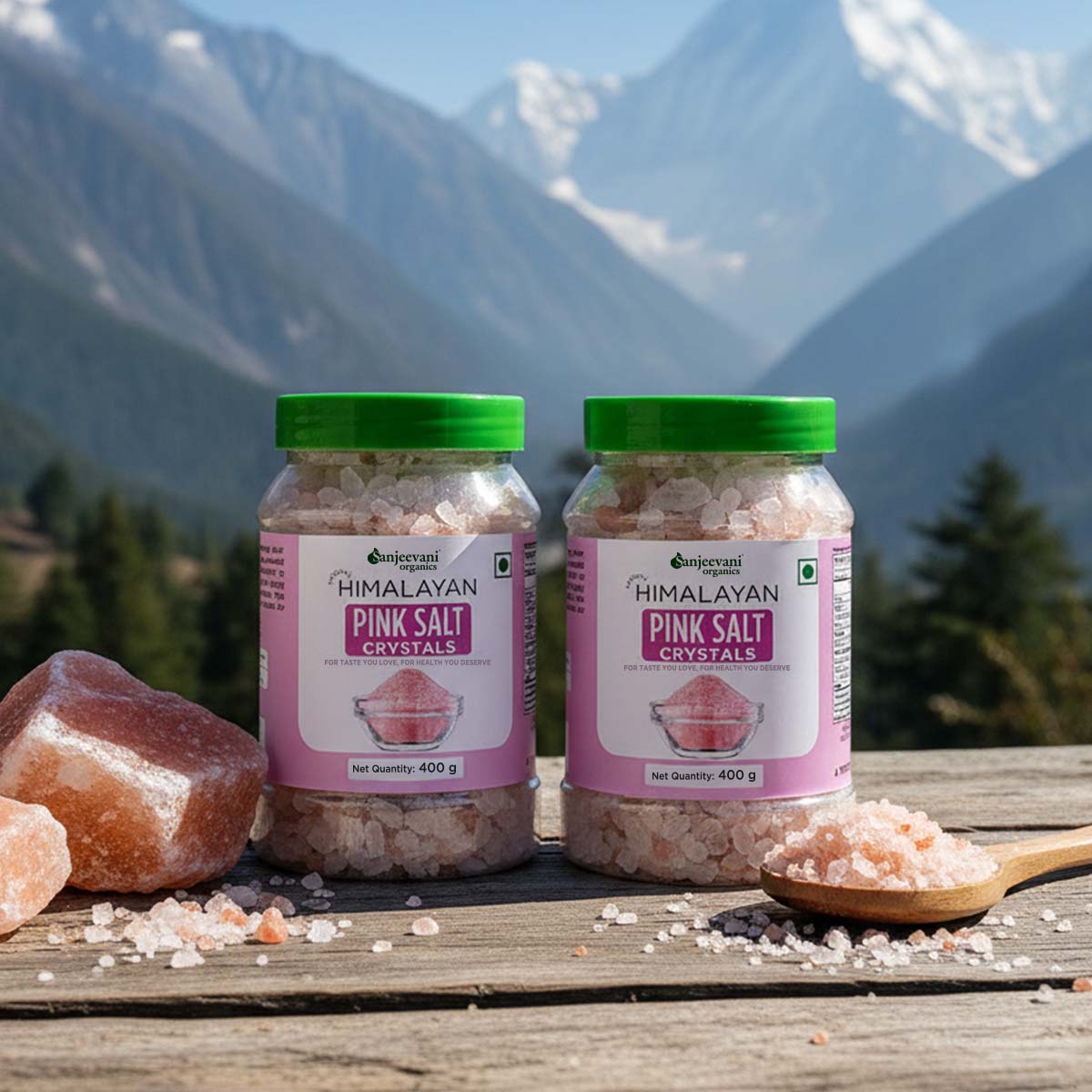 Barsana Magic and Two jars of Himalayan Pink Salt Crystals with pink salt crystals and a wooden spoon on a wooden surface with mountains in the background.
