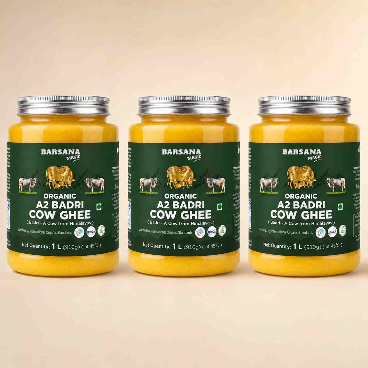 Barsana Magic and Three glass jars of Barsana Organic A2 Badri Cow Ghee arranged side by side on a light beige background. Each jar contains yellow ghee and has a dark green label with white text and illustrations of cows.