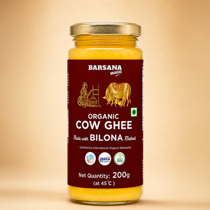 Barsana Magic andA 200g glass jar of Barsana Magic Organic Cow Ghee, made with Bilona Method, featuring a deep maroon label with gold illustrations and a gold metal lid, set against a warm beige background.