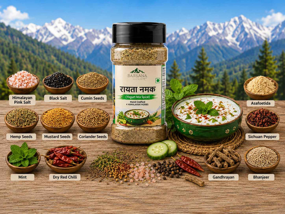 Barsana Magic and A jar of Rasavala Ayurvedic Whole Cooked Spicy Salt (Raktta Namak) centered on a wooden table, surrounded by labeled bowls and piles of its ingredients (pink salt, cumin seeds, hemp seeds, mustard seeds, coriander seeds, asafetida, sihuam pepper, mint, dry red chili, gandhrayan, and bharjun) against a backdrop of a mountain and pine forest.