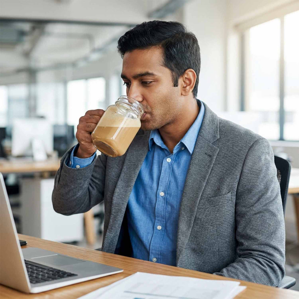 Barsana Magic and Man drinking from a jar of coffee while sitting at a desk in an office.