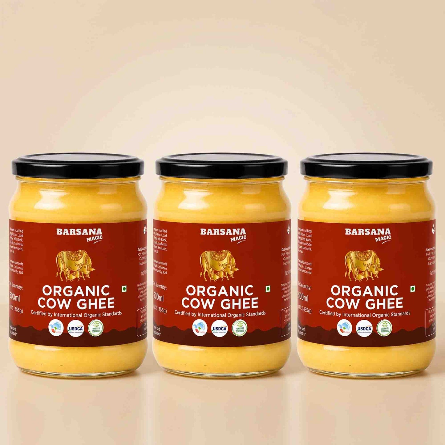 Barsana Magic and Three glass jars of Barsana Organic Cow Ghee with black lids and red labels, arranged side by side on a light beige background.