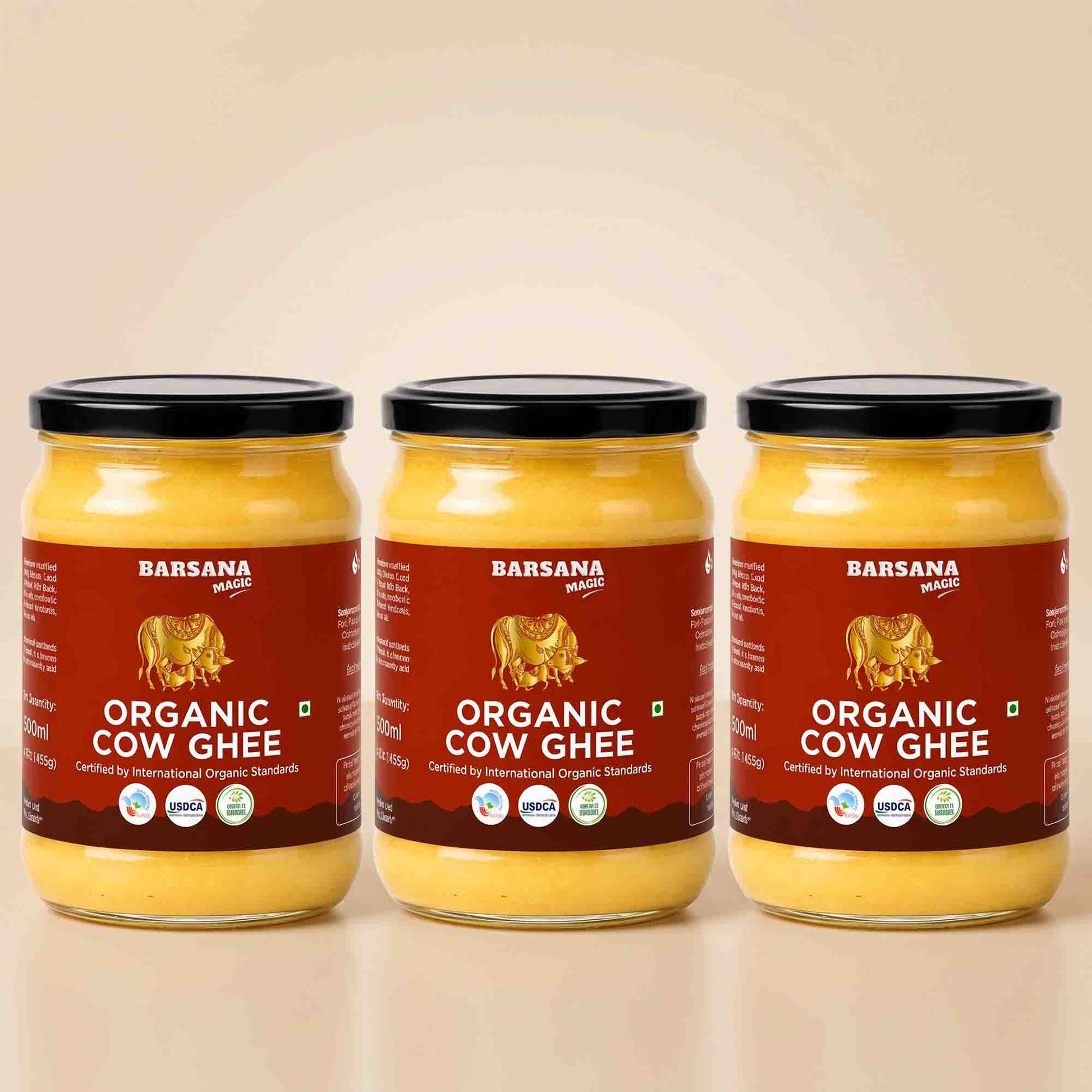 Barsana Magic and Three glass jars of Barsana Organic Cow Ghee with black lids and red labels, arranged side by side on a light beige background.