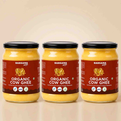 Barsana Magic and Three glass jars of Barsana Organic Cow Ghee with black lids and red labels, arranged side by side on a light beige background.
