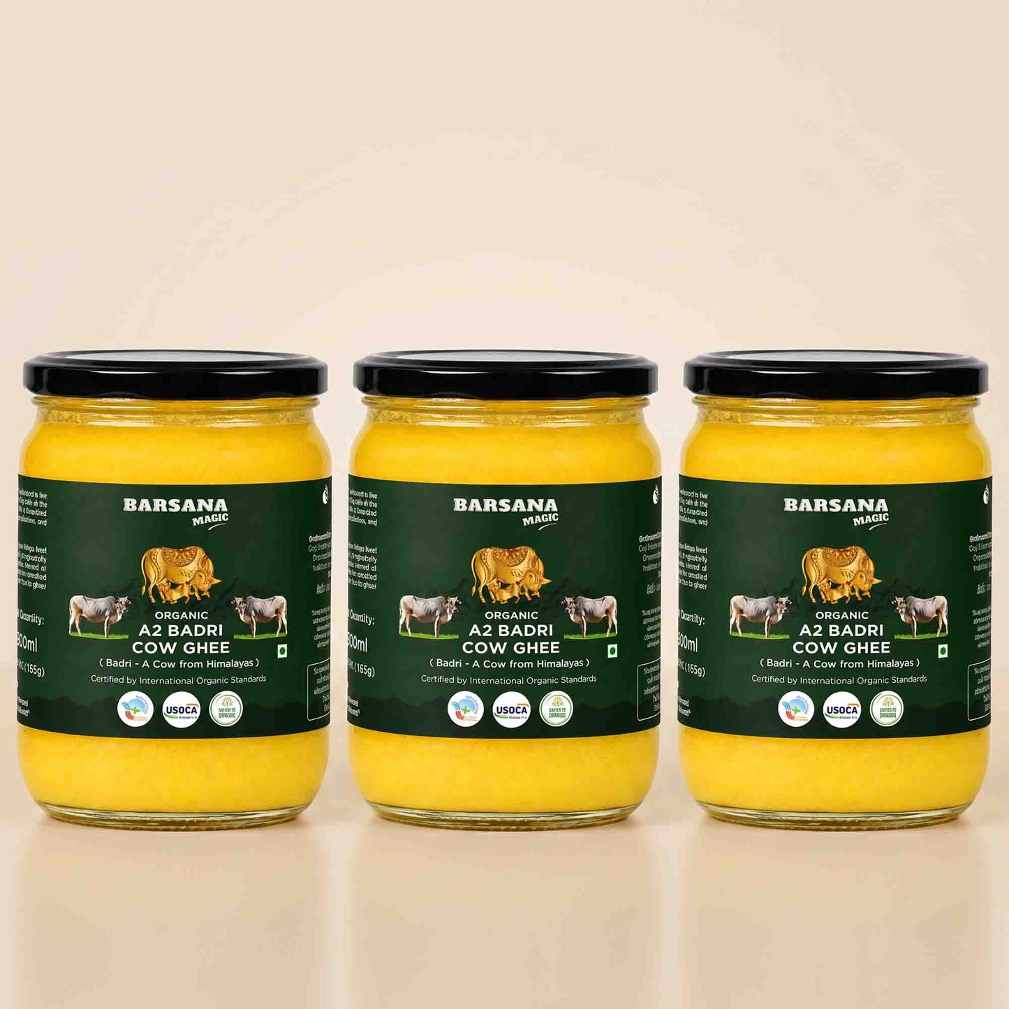Barsana Magic and Three glass jars of Barsana Organic A2 Badri Cow Ghee arranged side by side on a light beige background. Each jar contains bright yellow ghee and has a dark green label with black lids.