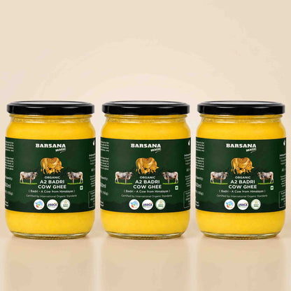 Barsana Magic and Three glass jars of Barsana Organic A2 Badri Cow Ghee arranged side by side on a light beige background. Each jar contains bright yellow ghee and has a dark green label with black lids.