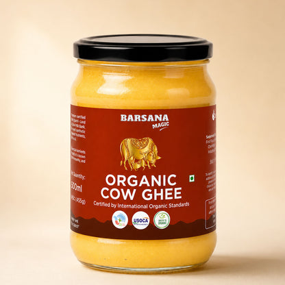Barsana Magic and A 500ml glass jar of Organic Cow Ghee, filled with yellow ghee and featuring a dark red label with a gold cow illustration and a black lid, set against a warm beige background.