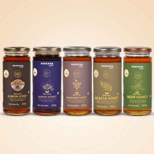 Barsana Magic and Five glass jars of BARSANA brand honey arranged in a row against a warm beige background. The jars have gold lids and labels in different colors: dark brown for Natural Ajwain Honey, purple for Natural Jamun Honey, brown for Natural Mustard Honey, olive green for Natural Acacia Honey, and dark green for Natural Neem Honey.