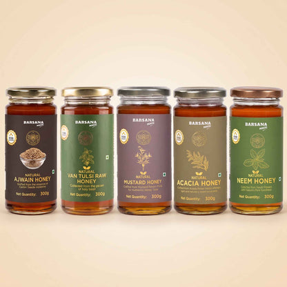 Barsana Magic and Five glass jars of BARANSA natural honey in different flavors and colors, lined up in a row against a warm beige background. The jars feature dark brown, green, purple, olive green, and dark green labels with gold lettering.