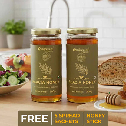 Barsana Magic and Two jars of Sanjeevani Acacia Honey on a table with a salad and bread in the background.