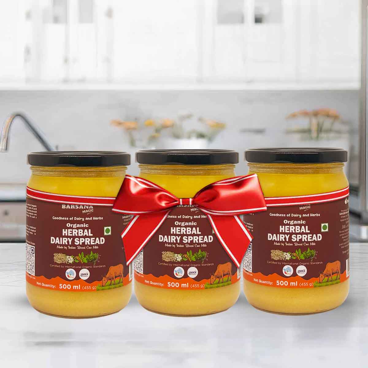 Barsana Magic and Three jars of organic herbal dairy spread with a red ribbon on a kitchen counter.