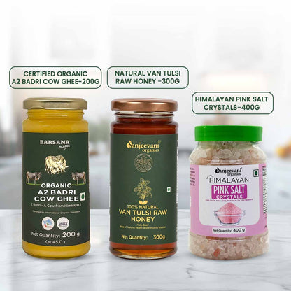Three bottles of organic products including Badri Cow Ghee, Van Tulsi Raw Honey, and Himalayan Pink Salt Crystals on a white background.