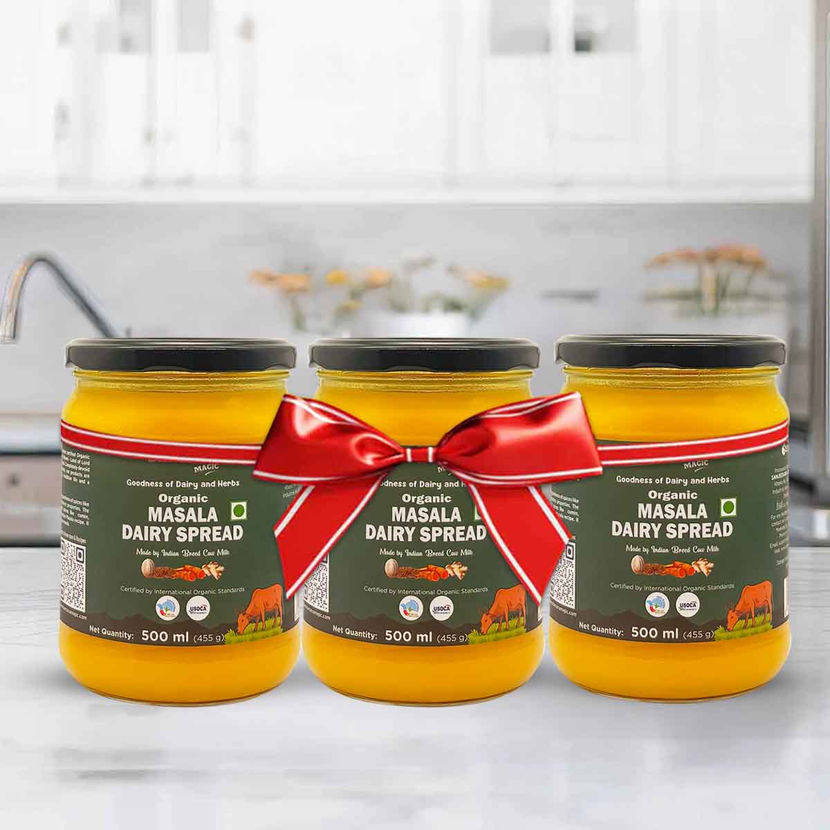 Barsana Magic and Three jars of Organic Masala Dairy Spread with a red ribbon on a kitchen counter.