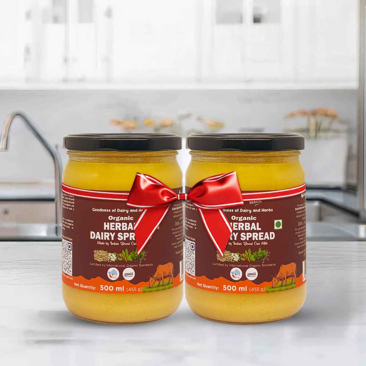 Barsana Magic and Two jars of organic herbal dairy spread with a red ribbon on a kitchen counter.