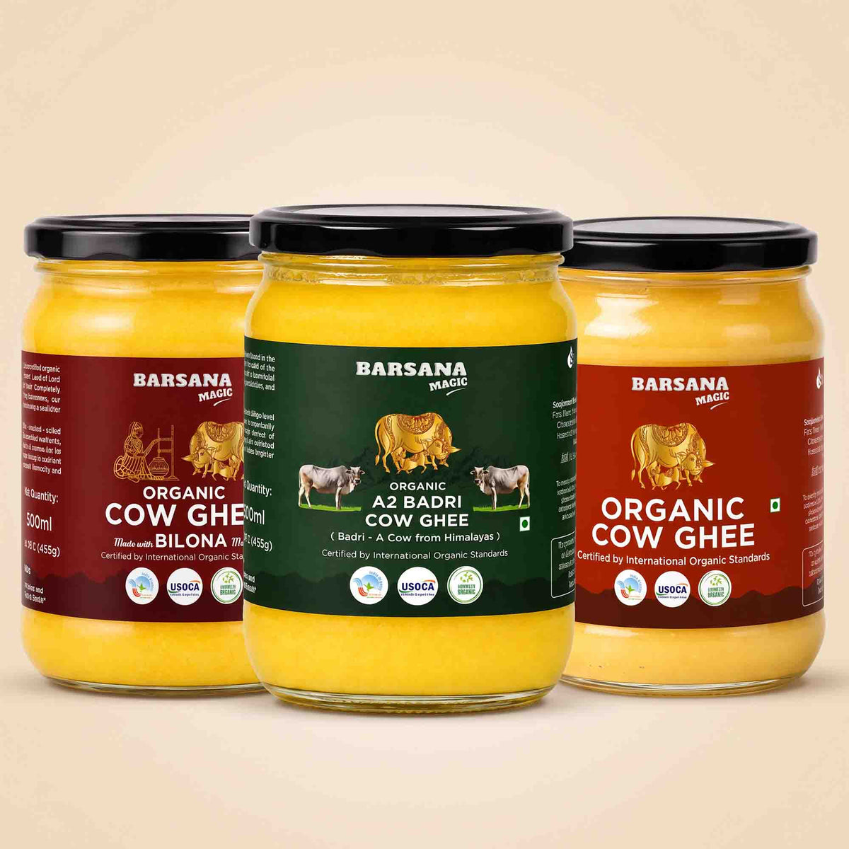 Barsana Magic and Three jars of Barsana Magic Organic Cow Ghee arranged together on a light beige background. The left jar has a maroon label, the center jar has a dark green label, and the right jar has a reddish-brown label, all showing the yellow ghee inside clear glass jars with black lids.