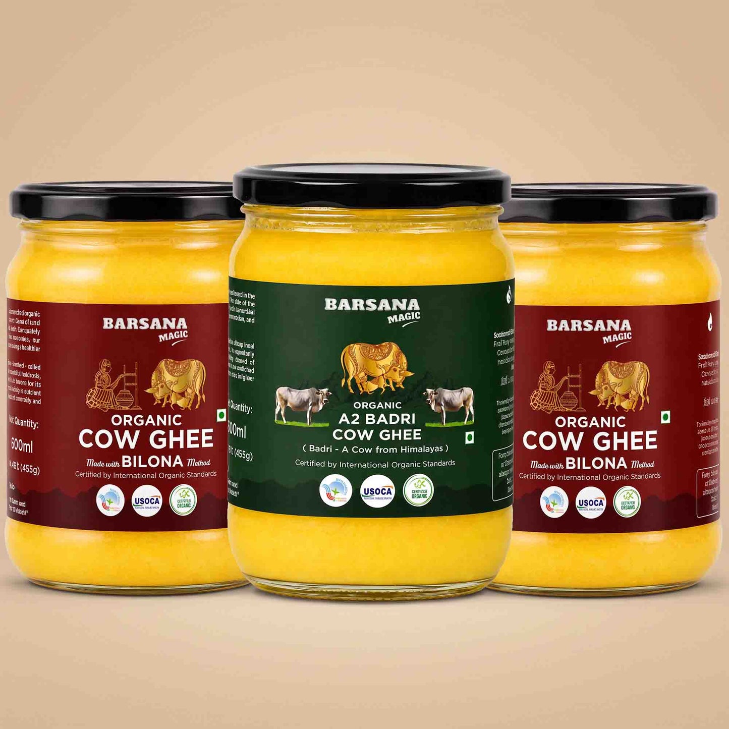 Barsana Magic and Three glass jars of Barsana Organic Cow Ghee arranged symmetrically on a warm beige background. The center jar has a dark green label, while the two side jars have dark red labels, all showing yellow ghee inside and black lids.