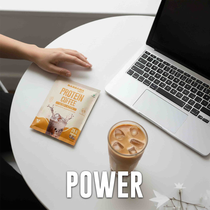 Barsana Magic and Barbells Protein Coffee package on a table with a glass of iced coffee and laptop, labeled 'POWER'.