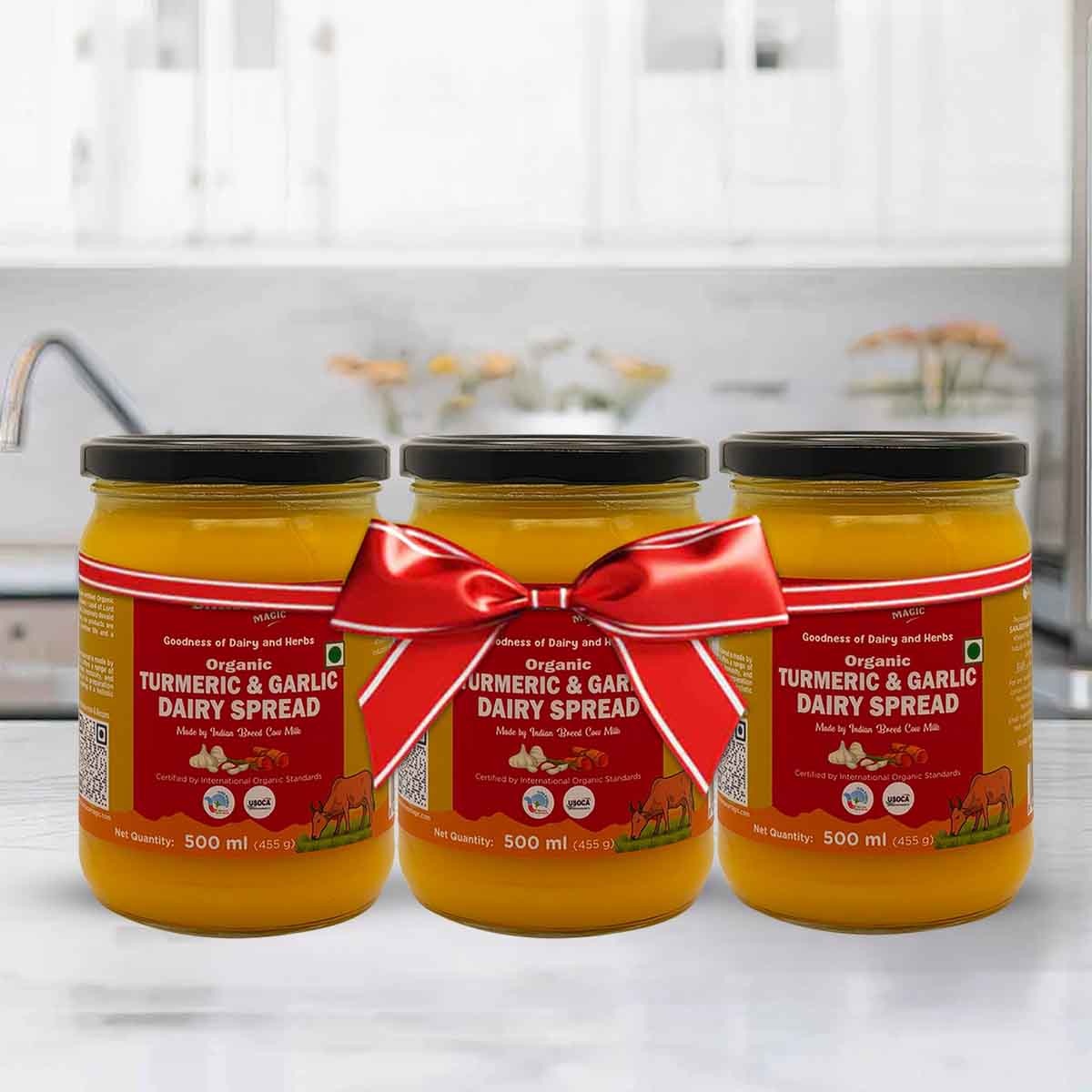 Barsana Magic and Three jars of Turmeric & Garlic Dairy Spread with a red ribbon on a kitchen counter.