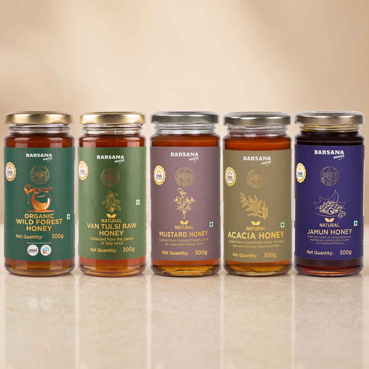 Barsana Magic and Five glass jars of BARSLANA pure honey lined up on a reflective surface against a warm beige background. The jars feature different colored labels: green for Organic Wild Forest Honey, olive green for Van Tulsi Raw Honey, purple for Natural Mustard Honey, brown for Acacia Honey, and dark purple for Natural Jamun Honey.