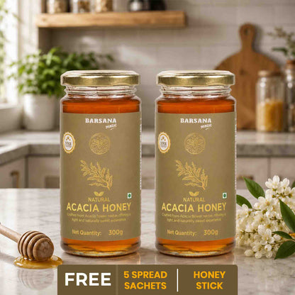 Barsana Magic and Two jars of Acacia Honey on a kitchen counter with a honey stick and flowers.