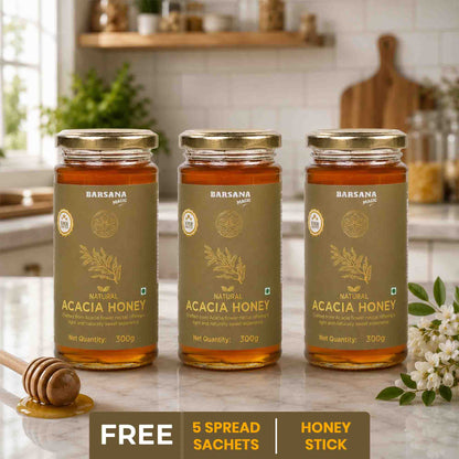 Barsana Magic and Three jars of Acacia Honey on a kitchen counter with a honey dipper and flowers.