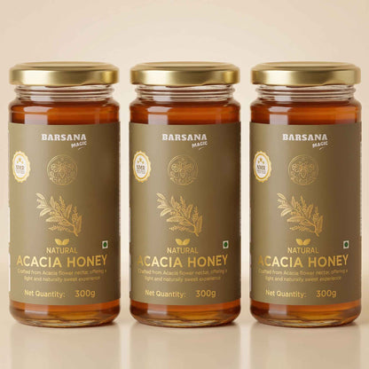 Barsana Magic and Three glass jars of Barsana Magic Natural Acacia Honey with gold lids and dark brown labels, arranged side by side on a light beige background.