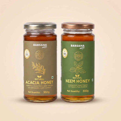 Barsana Magic and Two glass jars of Barsana Magic honey, Natural Acacia Honey on the left with a brown label and silver lid, and Natural Neem Honey on the right with a green label and bronze lid, set against a solid beige background.