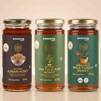 Barsana Magic and Three jars of Barsana Magic honey arranged side by side on a light beige background. The left jar is labeled Natural Ajwain Honey with a dark brown label and gold lid.