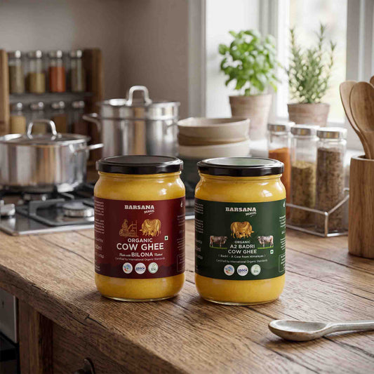 Barsana Magic and Two jars of Earsana Sansh cow ghee on a rustic wooden kitchen counter, with stainless steel pots, spice jars, and potted plants in the softly blurred background.