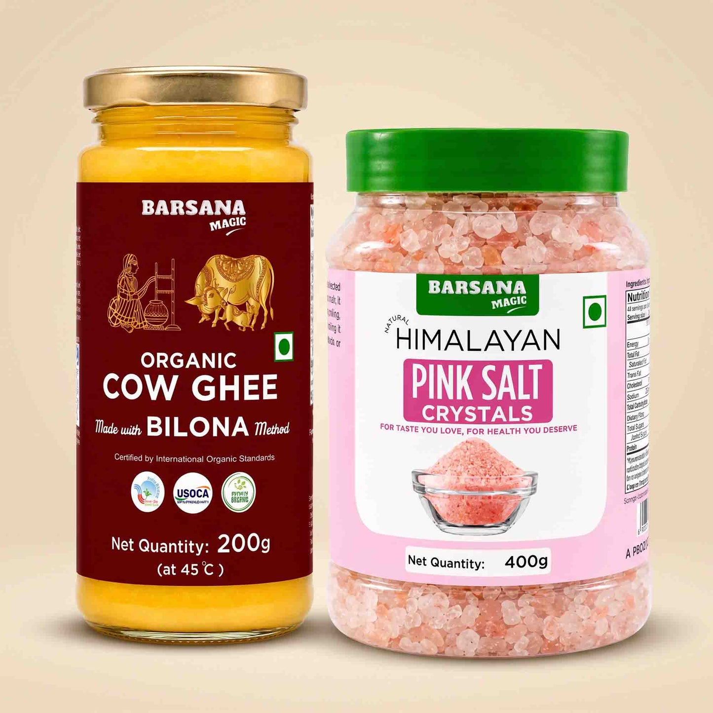 Barsana Magic and Two jars of Barsana Magic brand food products on a beige background: a 200g jar of Organic Cow Ghee with a gold lid and dark red label, and a 400g jar of Himalayan Pink Salt Crystals with a green lid and pink label.