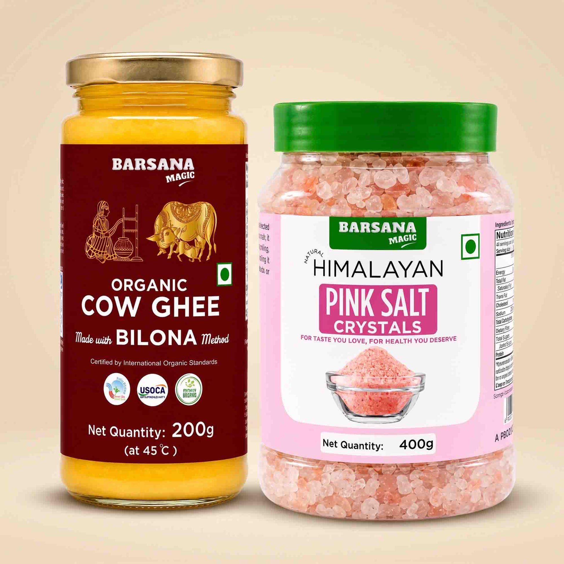 Barsana Magic and Two jars of Barsana Magic brand food products on a beige background: a 200g jar of Organic Cow Ghee with a gold lid and dark red label, and a 400g jar of Himalayan Pink Salt Crystals with a green lid and pink label.