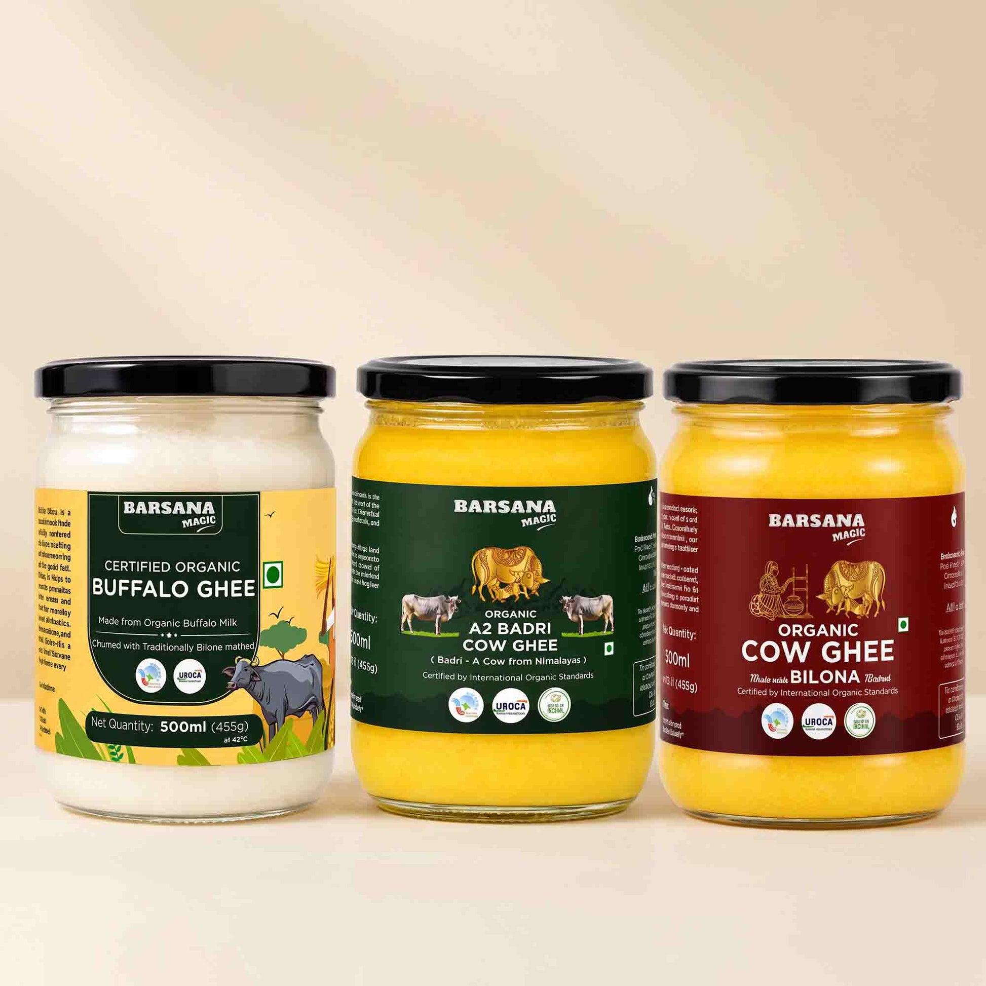 Barsana Magic and Three glass jars of Barsana brand ghee arranged side by side on a light beige background. The left jar contains Certified Organic Buffalo Ghee with a yellow label, the middle jar contains A2 Badri Cow Ghee with a dark green label, and the right jar contains Organic Cow Ghee with a dark red label.