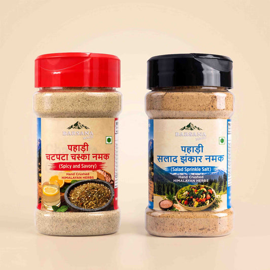 Barsana Magic and Two jars of Himalayan Herb ground spices on a light beige background. The left jar has a red lid and is labeled 'Pahadi Chappata Masala Namak' (Spicy and Savory), and the right jar has a black lid and is labeled 'Pahadi Salad Zikkar Namak' (Salad Sprinkle Salt).