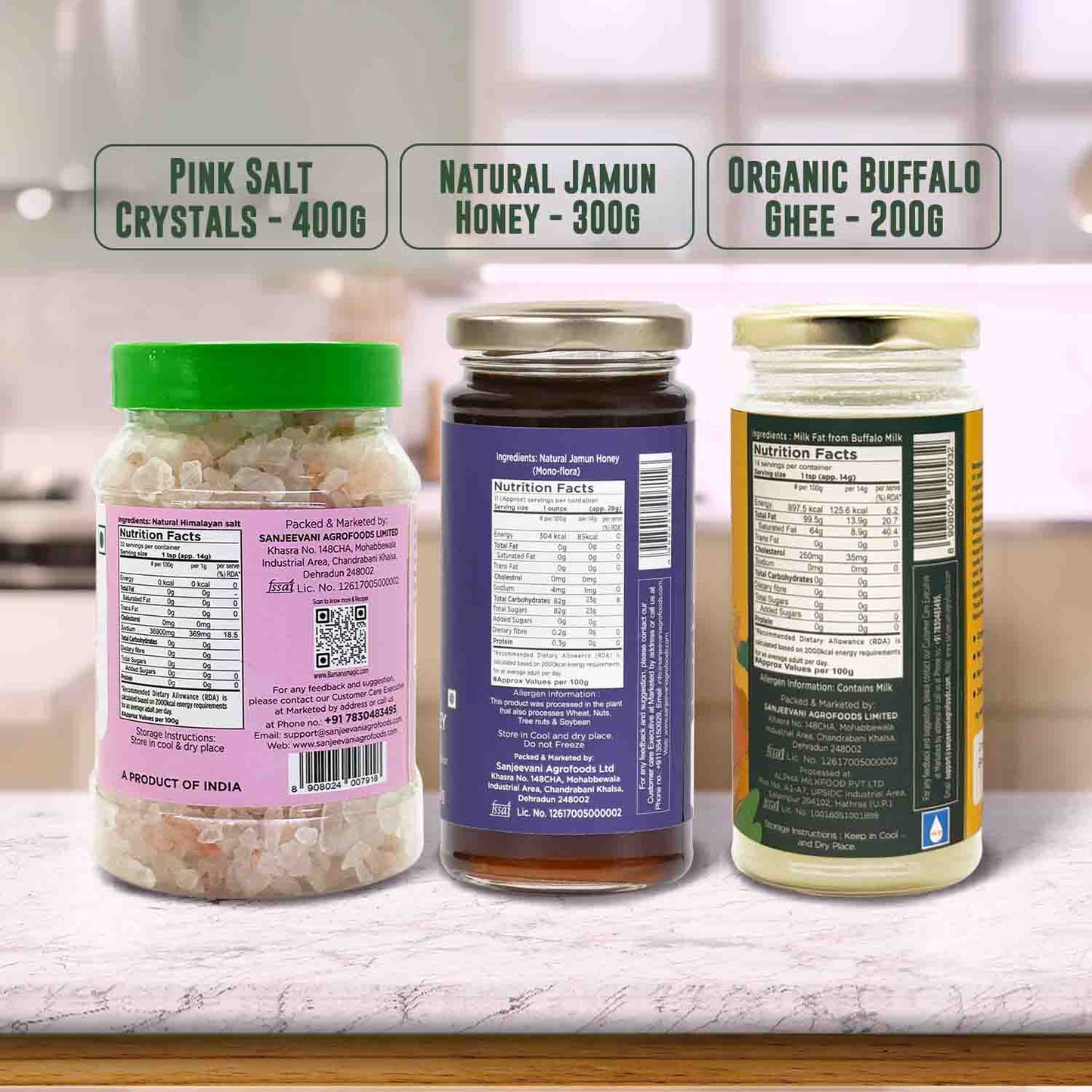 Barsana Magic and Three jars with labels for Pink Salt Crystals, Natural Jamun Honey, and Organic Buffalo Ghee on a blurred kitchen background.