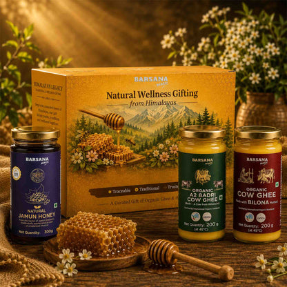 Barsana Magic and A BarSana Wellness gift set featuring three jars of organic honey and cow ghee arranged in front of a decorative wooden box on a rustic wooden surface with flowers and honeycomb props.