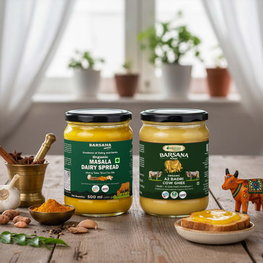 Barsana Magic and Two jars of Barsana organic dairy spread on a wooden table with a window and plants in the background.