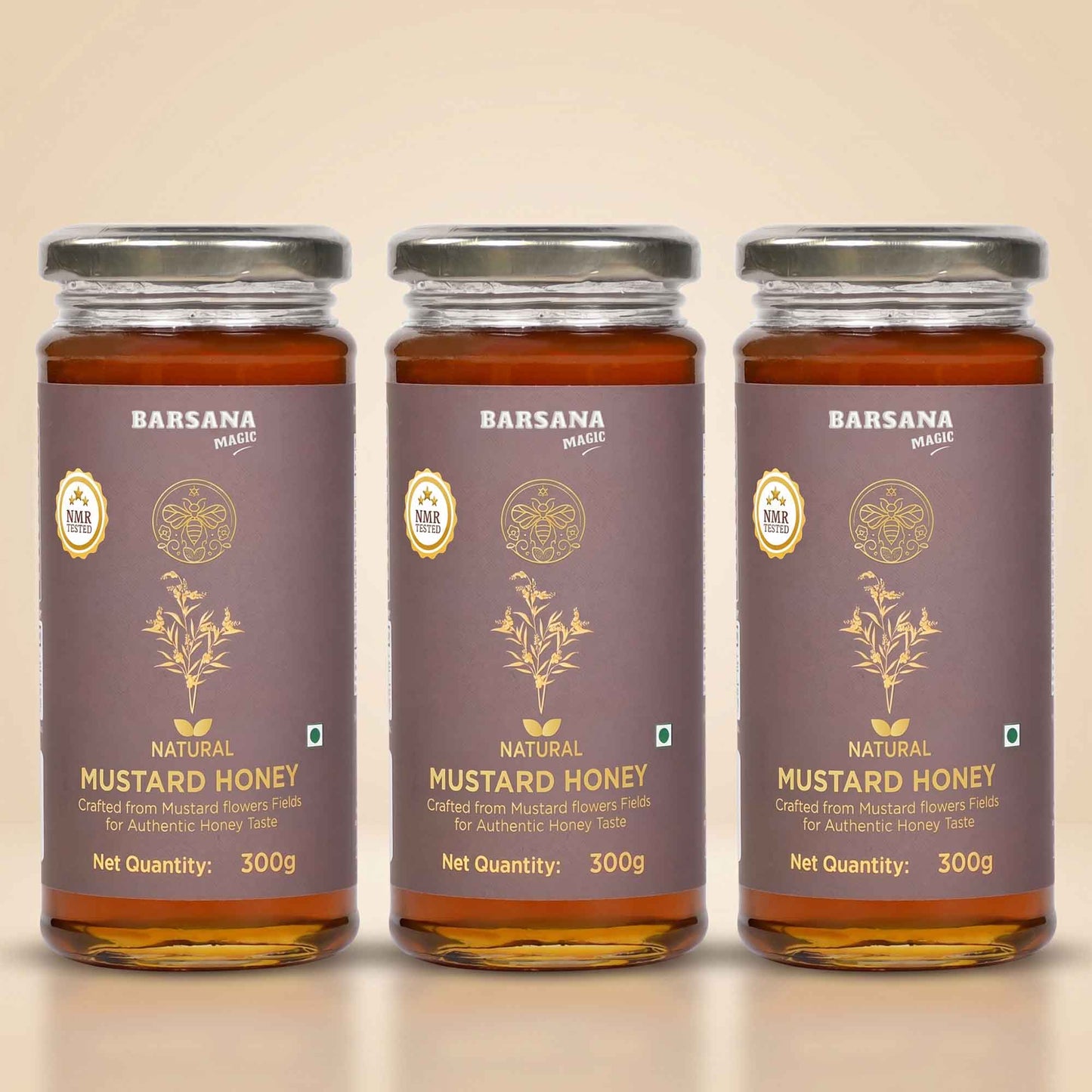 Barsana Magic and Three glass jars of Barsana Magic Natural Mustard Honey arranged side by side on a light beige background. Each jar contains amber-colored honey and has a dark brown label with gold text and illustrations, topped with a silver metal lid.