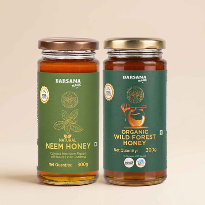 Barsana Magic and Two glass jars of Barsana Magic honey on a light beige background. The left jar is labeled 'Natural Neem Honey' with a green label and a bronze lid, and the right jar is labeled 'Organic Wild Forest Honey' with a green label and a gold lid.