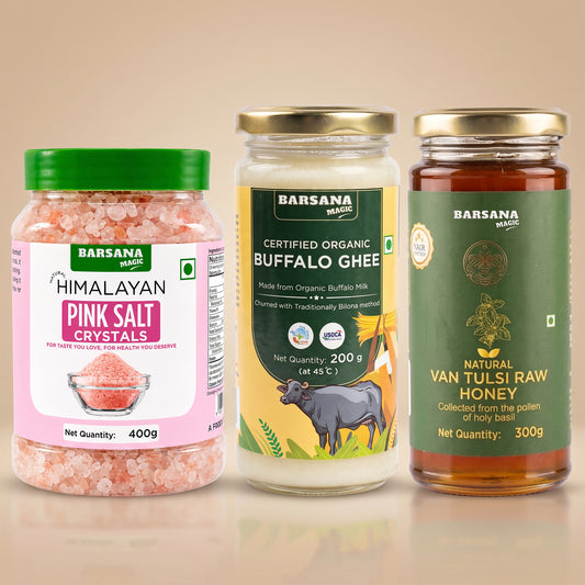 Barsana Magic and Three jars of Barsana brand household products arranged side by side on a beige background: a pink Himalayan salt crystal jar with a green lid, a buffalo ghee jar with a yellow and green label, and a raw honey jar with a dark green label.