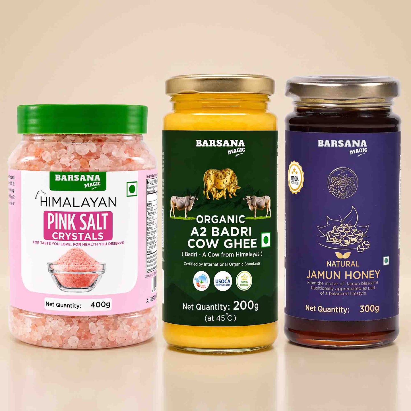 Barsana Magic and Three jars of Barsana Magic brand products arranged side-by-side on a reflective beige surface: Himalayan Pink Salt Crystals, Organic A2 Badri Cow Ghee, and Natural Jamun Honey.