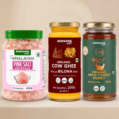 Barsana Magic and Three Barsana Magic products displayed side-by-side on a beige surface: Himalayan Pink Salt Crystals in a clear jar with a green lid, Organic Cow Ghee in a yellow jar with a gold lid, and Organic Wild Forest Honey in a dark green jar with a gold lid.