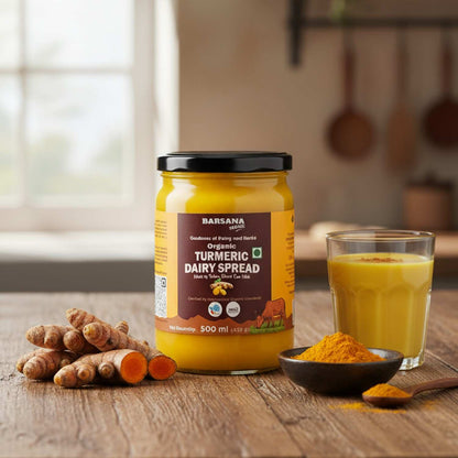 Barsana Magic and Jar of Turmeric Dairy Spread on a wooden table with turmeric roots and a glass of juice.