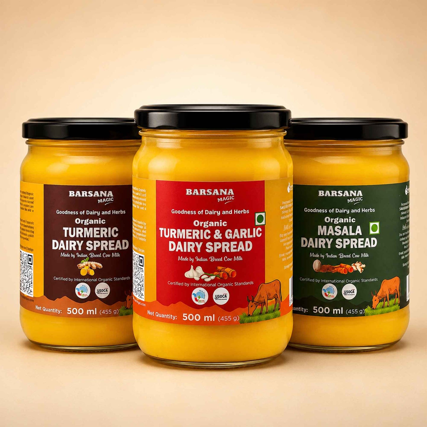 Barsana Magic and Three glass jars of Barsana Masala Dairy Spread arranged in a row on a beige background. The left jar is Organic Turmeric Dairy Spread with a dark brown label, the center jar is Organic Turmeric & Garlic Dairy Spread with a red label, and the right jar is Organic Masala Dairy Spread with a dark green label.