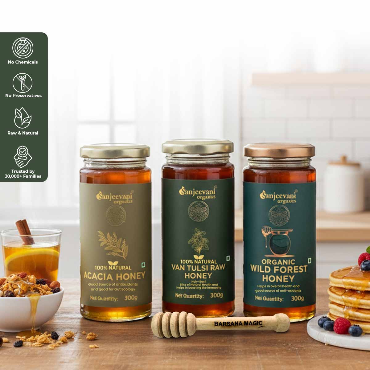 Barsana Magic and Three jars of Sanjeevani Organics honey on a wooden table with a glass of honey and pancakes in the background.