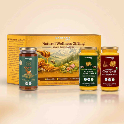 Barsana Magic and Legacy Natural Wellness Gifting set featuring a large yellow box and three glass jars of organic honey, cow ghee, and bilona milk powder arranged on a reflective white surface against a warm beige background.