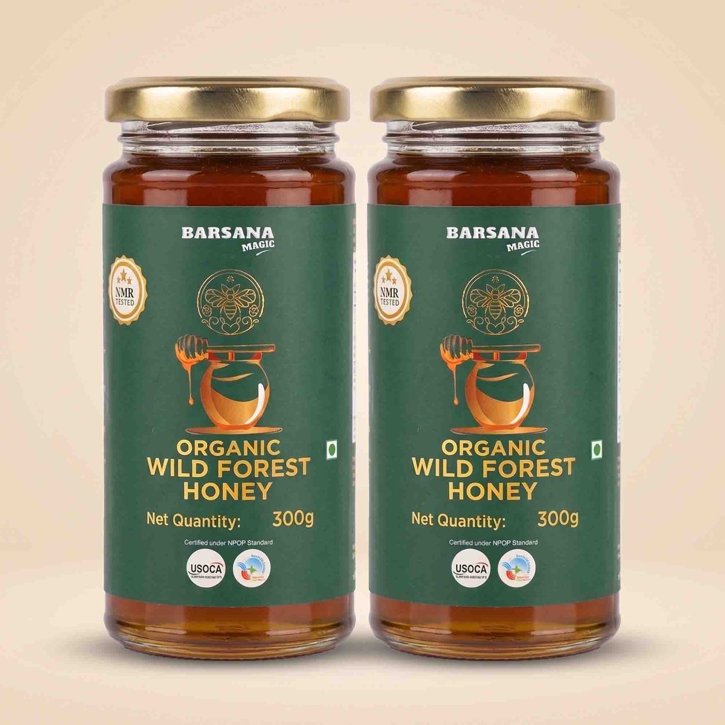 Barsana Magic and Two glass jars of Barsana Handmade Organic Wild Forest Honey with gold lids and dark green labels, displayed side-by-side on a light beige background.